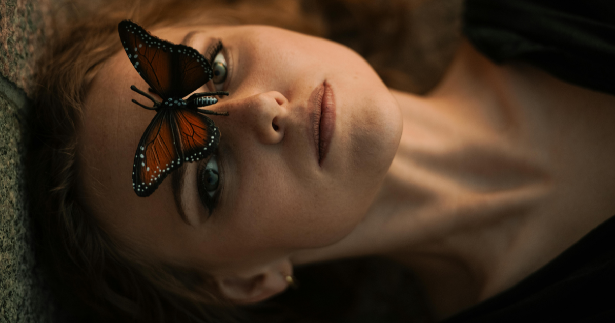 Woman lying peacefully with a butterfly on her forehead, symbolizing personal transformation and awakening.